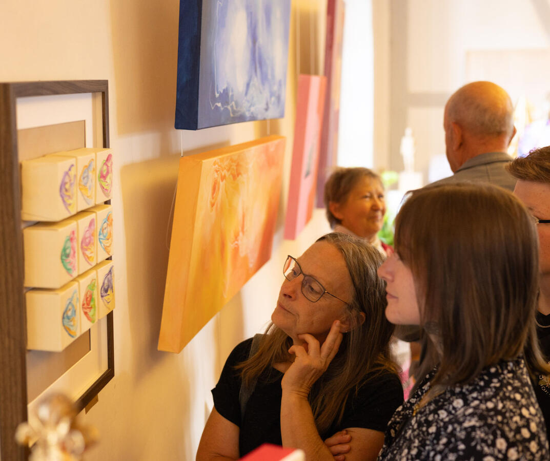 Mehrere Besucher der Vernissage betrachten ein Kunstwerk an der Wand