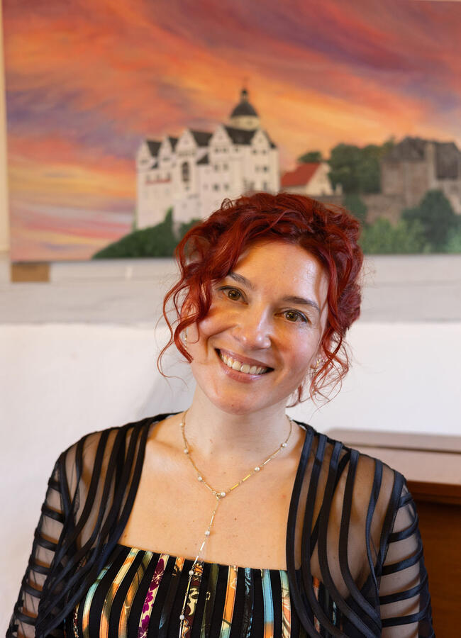 Die Pianistin und Malerin Yuliya Drogalova steht vor ihrem Burg Ranis Gemälde