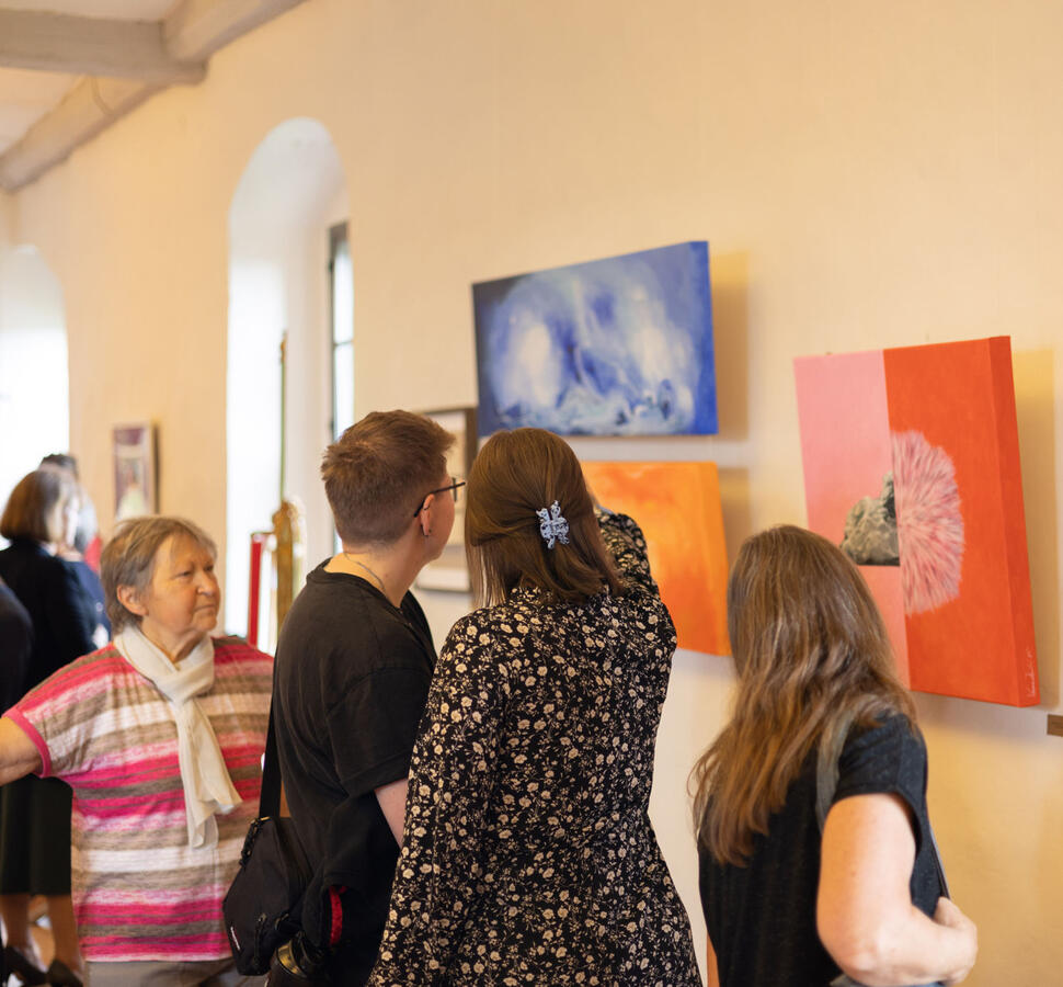 Vier Besucher der Ausstellung betrachten die Kunstwerke und diskutieren darüber