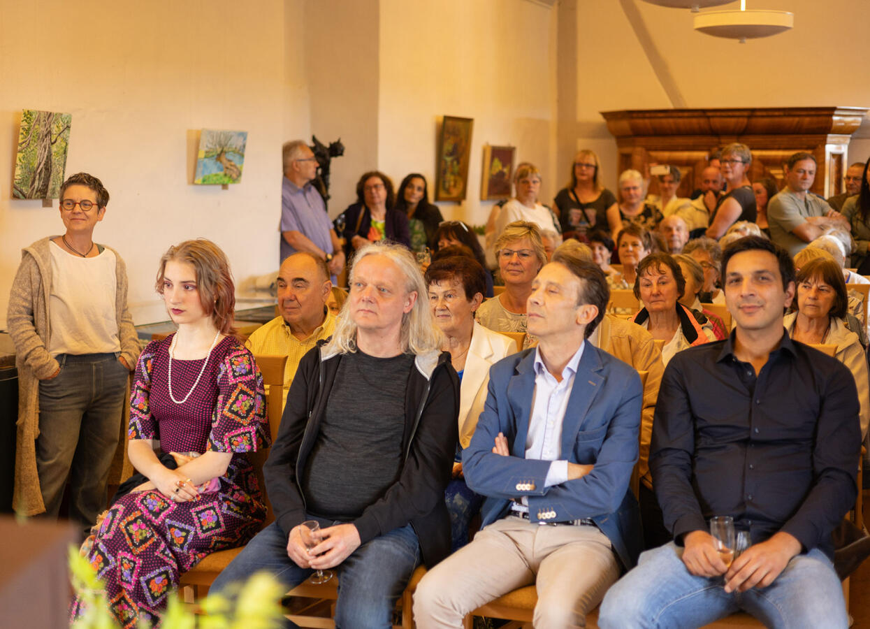 Künstler und Gäste sitzen auf Stühlen und hören dem KlavierKonzert zu