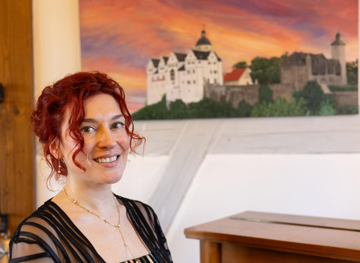 Die Pianistin Yuliya Drogalova steht vor ihrem Gemälde der Burg Ranis