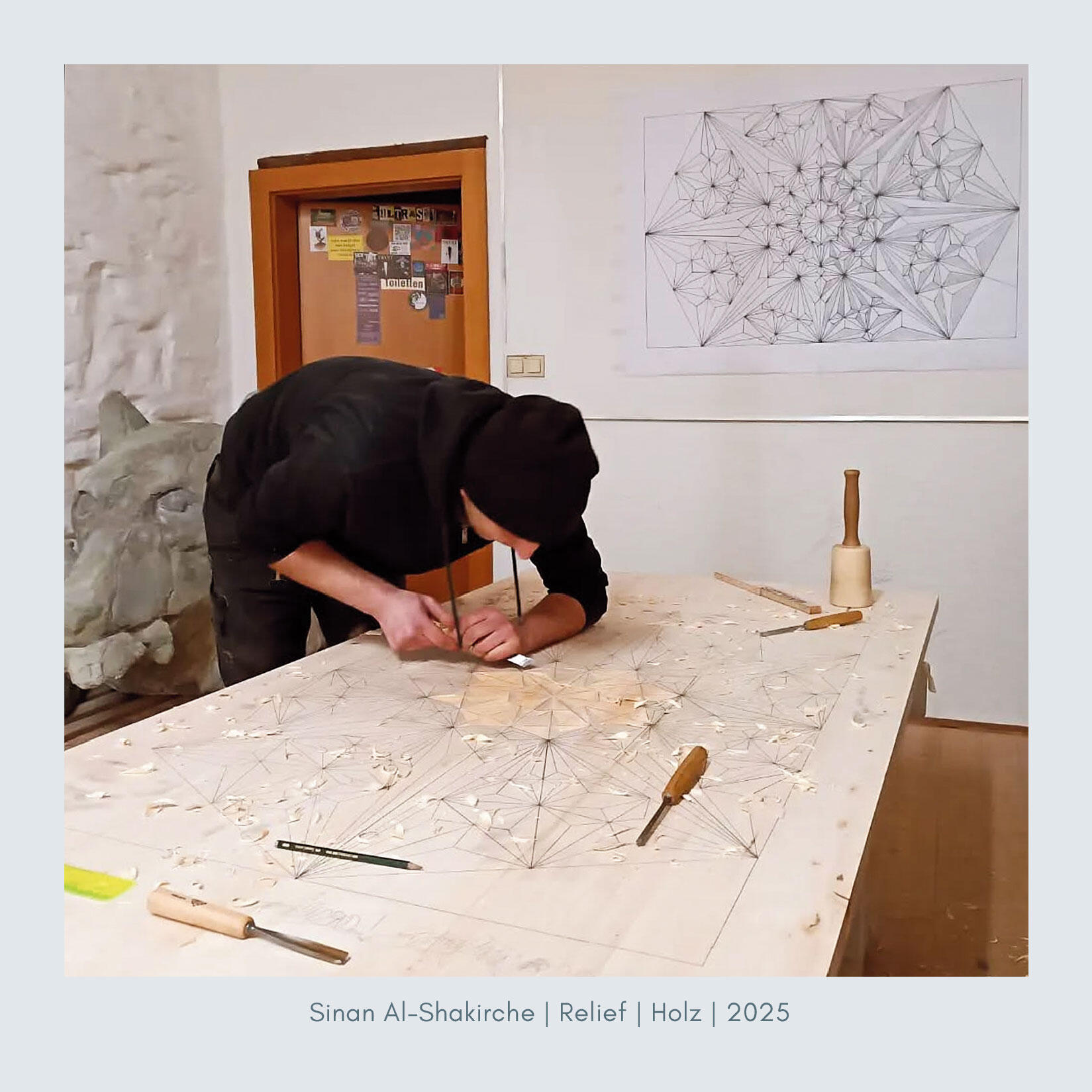 Relief Künstler Sinan Al-Shakirche arbeitet konzentriert an einem geometrischen Holzrelief. Auf dem großen Holztisch sind Schnitzwerkzeuge verteilt, an der Wand hängt eine Skizze des Musters. Werk aus dem Jahr 2025.